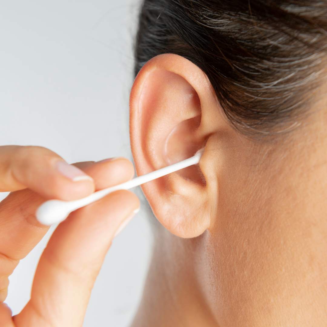 A person using a cotton swab to clean the outer area of their ear.