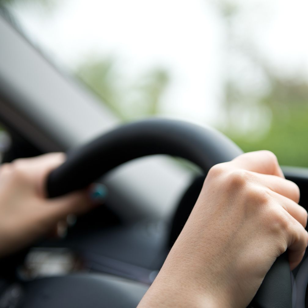 A persons hands gripping a car steering wheel.